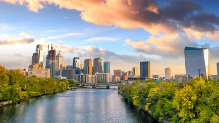 A scenic view of the Philadelphia skyline at sunset reflected over a tree-lined river, highlighting the convenient proximity of Arbor Terrace to dementia care resources near the Philadelphia metro area.