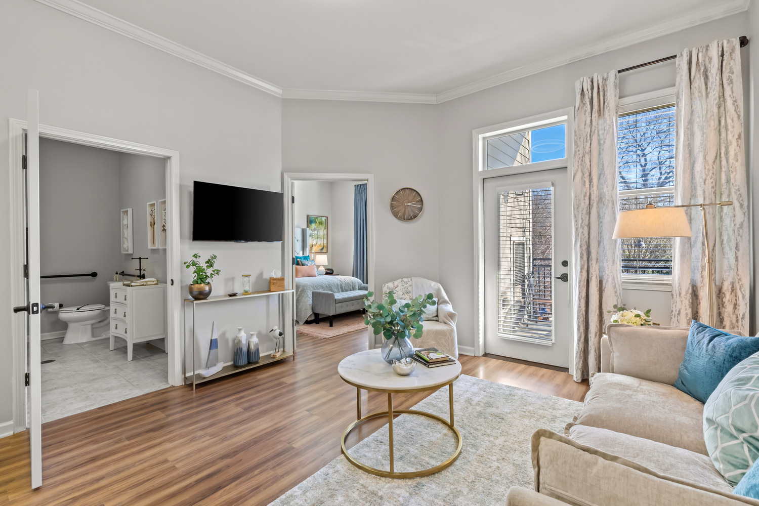 A bright and thoughtfully designed model apartment at this Acworth senior living community, featuring a living area with soft furnishings, a flat-screen TV, and large windows with natural light.