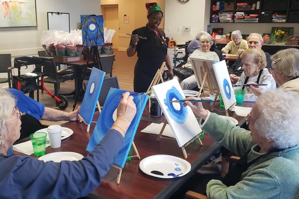 Residents participate in a group painting class led by a staff member, showcasing the creative and engaging senior lifestyle programs offered at this Acworth, GA senior living community.