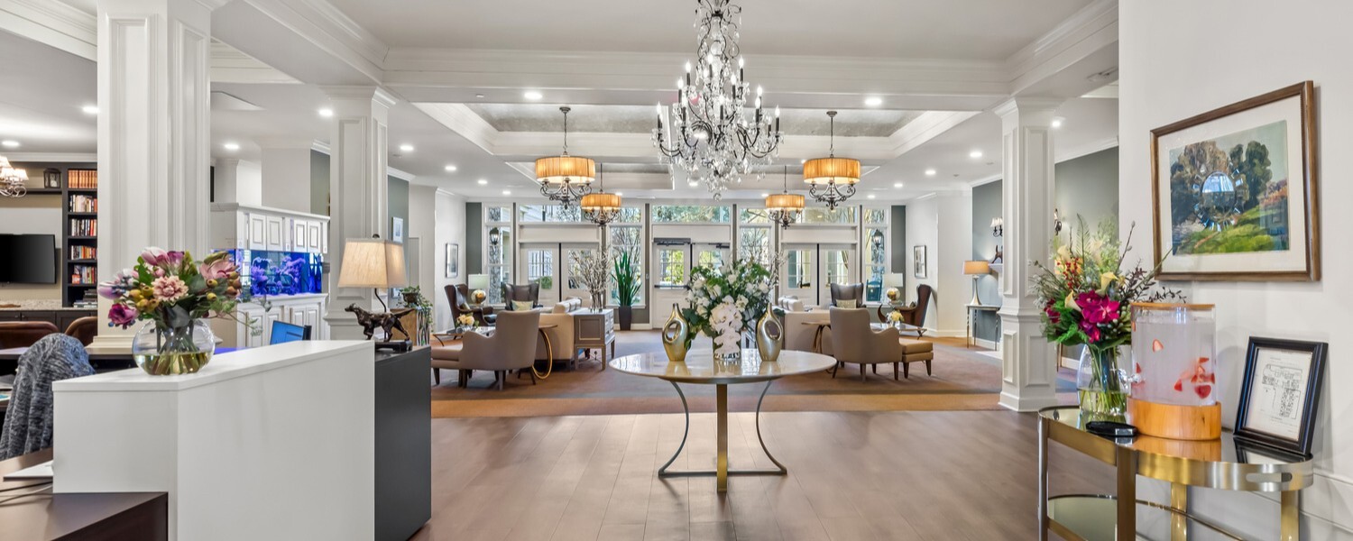 The bright, elegantly appointed lobby of this senior living community in Acworth, GA, featuring a chandelier, fresh floral arrangements, and open dining and lounge spaces bathed in natural light.