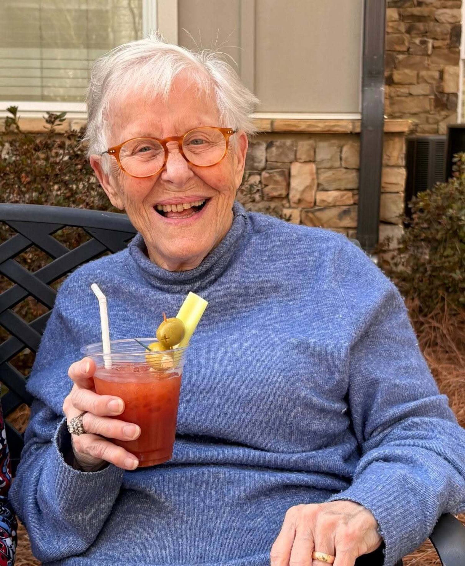 Resident laughing while enjoying a drink outdoors on a patio at our senior living community in Acworth, GA, part of our resort-style senior amenities