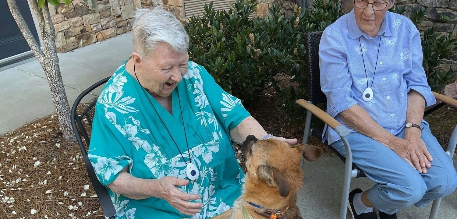 Resident enjoying a visit with a friendly dog outdoors at our pet-friendly senior living community in Acworth, GA, surrounded by lush garden greenery