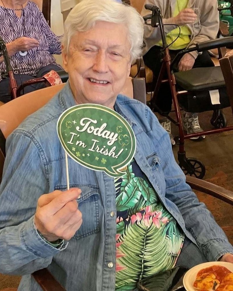 Resident smiling while holding a festive green pin during a themed celebration at our senior living community in Acworth, GA, part of our engaging senior lifestyle programs