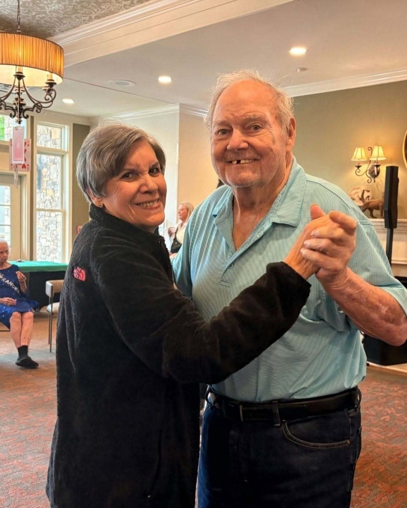 A couple dances together happily in a bright common area, enjoying connection and an active senior lifestyle at The Arbor Company.
