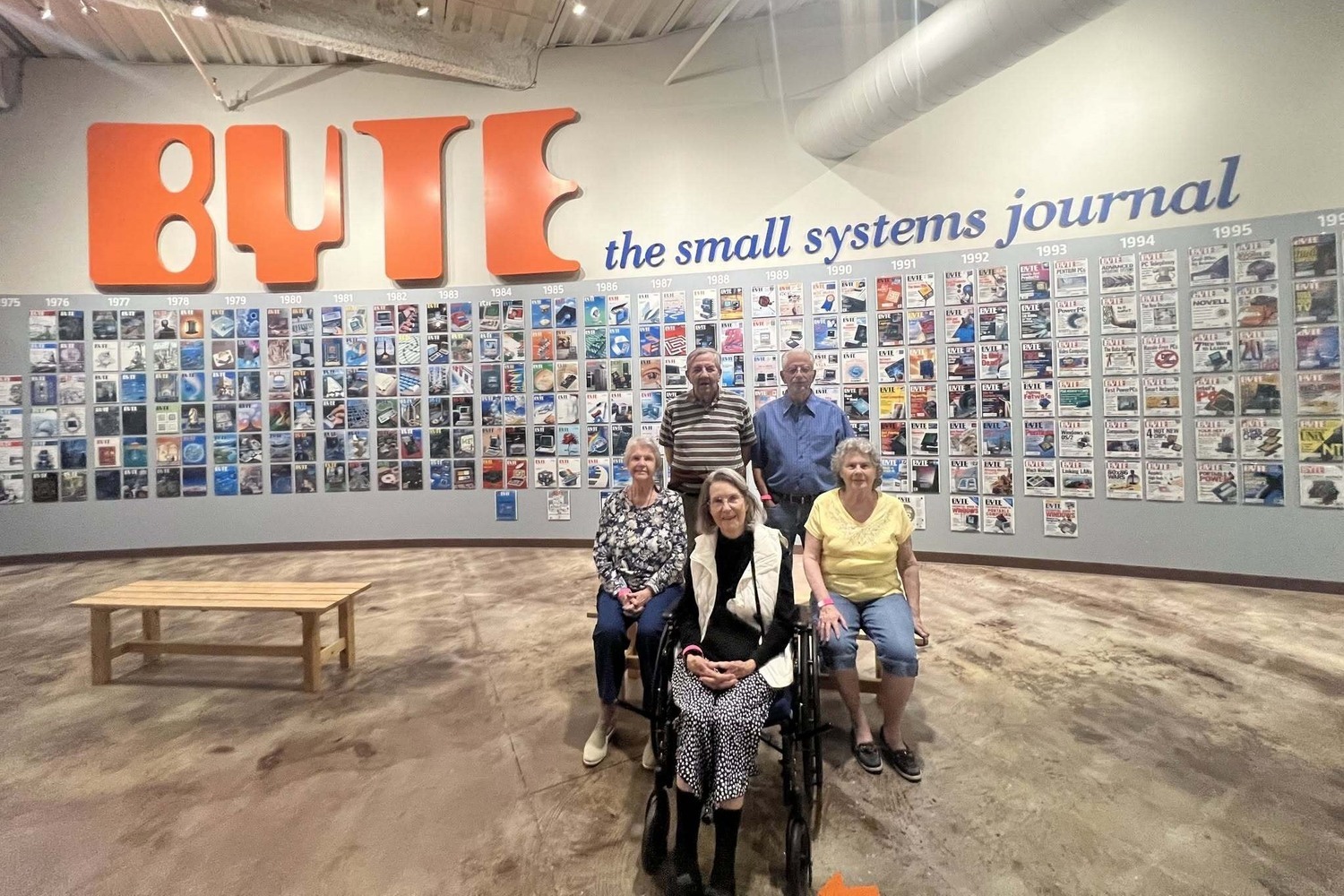 A group of residents pose together indoors at a tech history museum, enjoying a fun outing that reflects the active senior lifestyle and community connection at The Arbor Company.