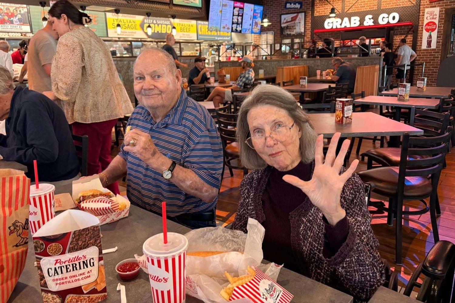 Two residents share a laugh over lunch at a casual restaurant, enjoying a lively outing as part of an active senior lifestyle at The Arbor Company.
