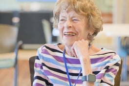 A woman smiles warmly while seated in a bright, open common area, radiating the joy and sense of belonging found in senior living in Athens, GA at Arbor Terrace of Athens.