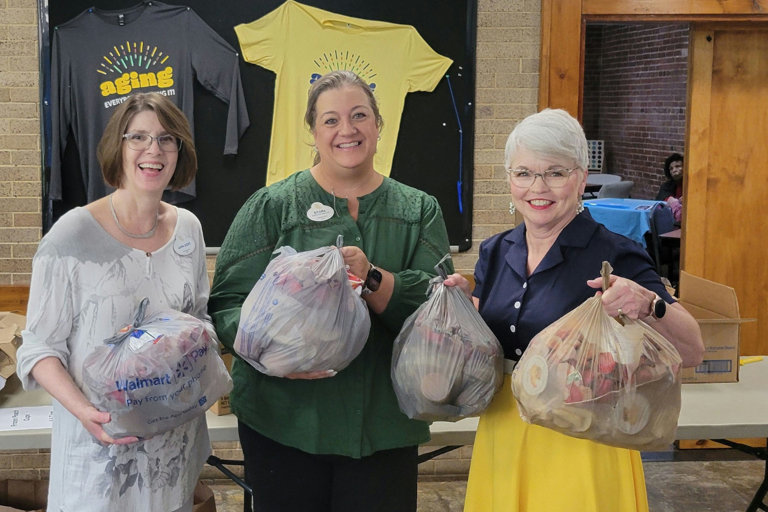 Two smiling staff members at Arbor Terrace Athens holding donated goods, reflecting the community's warm spirit and commitment to giving back — a hallmark of senior living in Athens, GA.
