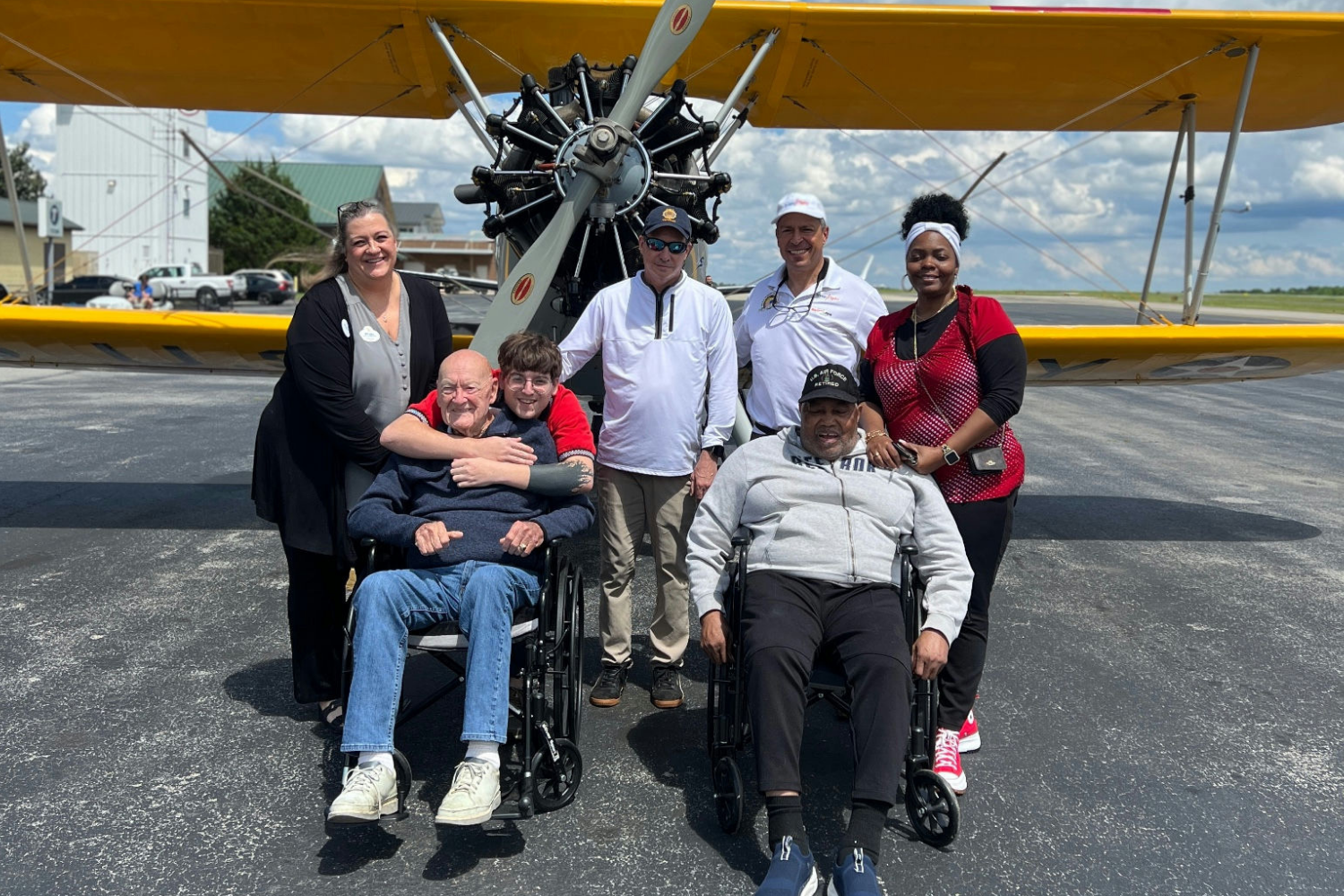 A cheerful group of residents and staff posing in front of a vintage aircraft at Arbor Terrace Athens, capturing the active lifestyle and fun outings enjoyed at this senior living community in Athens, GA.