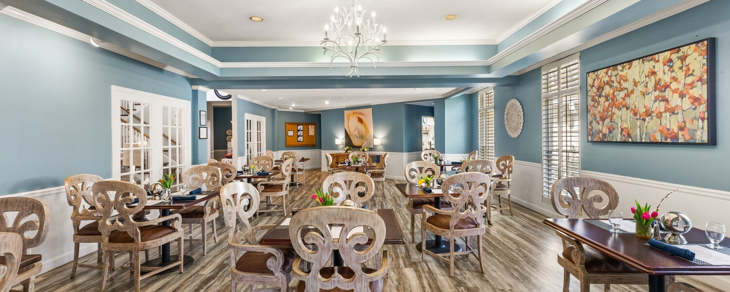An elegant dining room with blue walls, a crystal chandelier, and wood flooring at Arbor Terrace Athens, a senior living community in Athens, GA, reflecting resort-style senior living in Athens, GA.