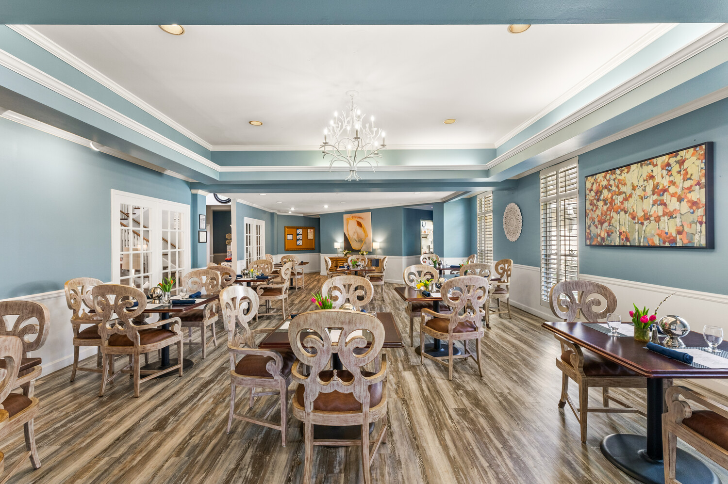 A spacious dining room at Arbor Terrace Athens with elegant chandeliers, decorative chairs, and soft blue walls, providing a warm gathering place for residents of this senior living community in Athens, GA.