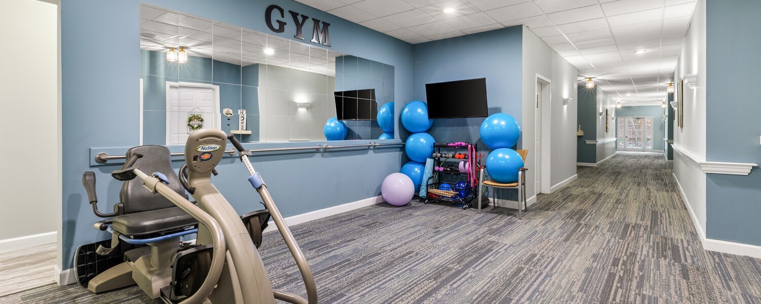 A fitness room at Arbor Terrace Athens features exercise equipment, stability balls, and a wall-mounted TV, supporting an active senior living lifestyle in Athens, GA.