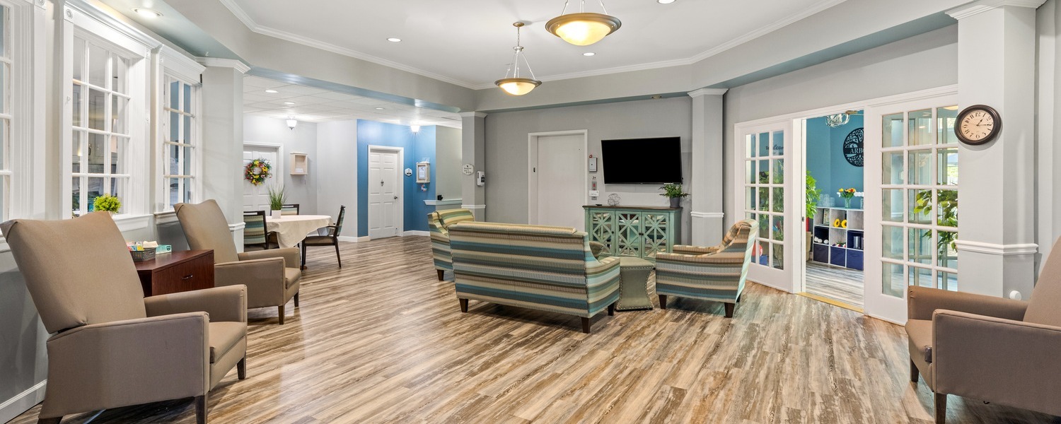 A cozy common area at Arbor Terrace Athens, a senior living community in Athens, GA, with soft seating, a mounted TV, and warm wood-look flooring, ideal for active senior living in Athens, GA.