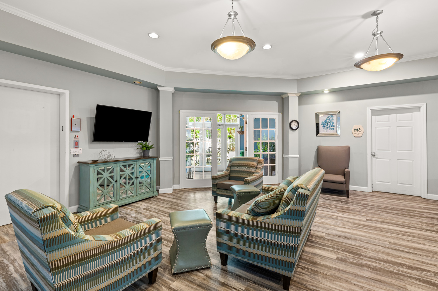 A welcoming circular living space in the memory care neighborhood at Arbor Terrace Athens, with cozy patterned chairs, soft teal tones, and a wall-mounted TV, thoughtfully designed for Alzheimer's care in Athens, GA.