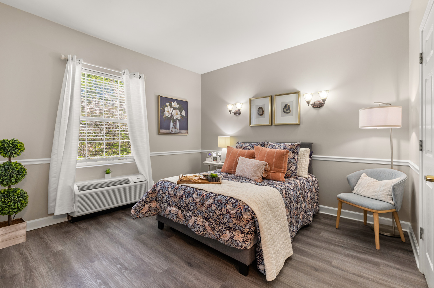 A beautifully appointed model apartment at Arbor Terrace Athens featuring a cozy bed with warm accents, soft wall sconces, and tasteful decor, showcasing comfortable resident living at this senior community in Athens, GA.