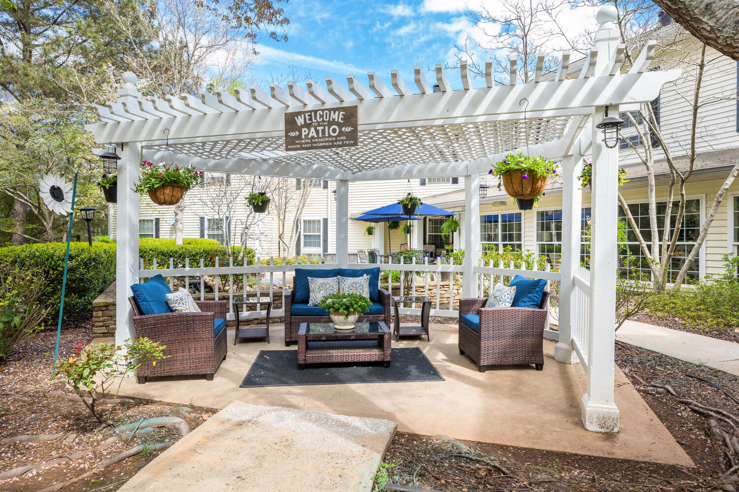 A charming outdoor patio at Arbor Terrace Athens featuring a pergola, comfortable seating with blue cushions, and hanging flower baskets, a welcoming spot for residents enjoying outdoor senior living in Athens, GA.