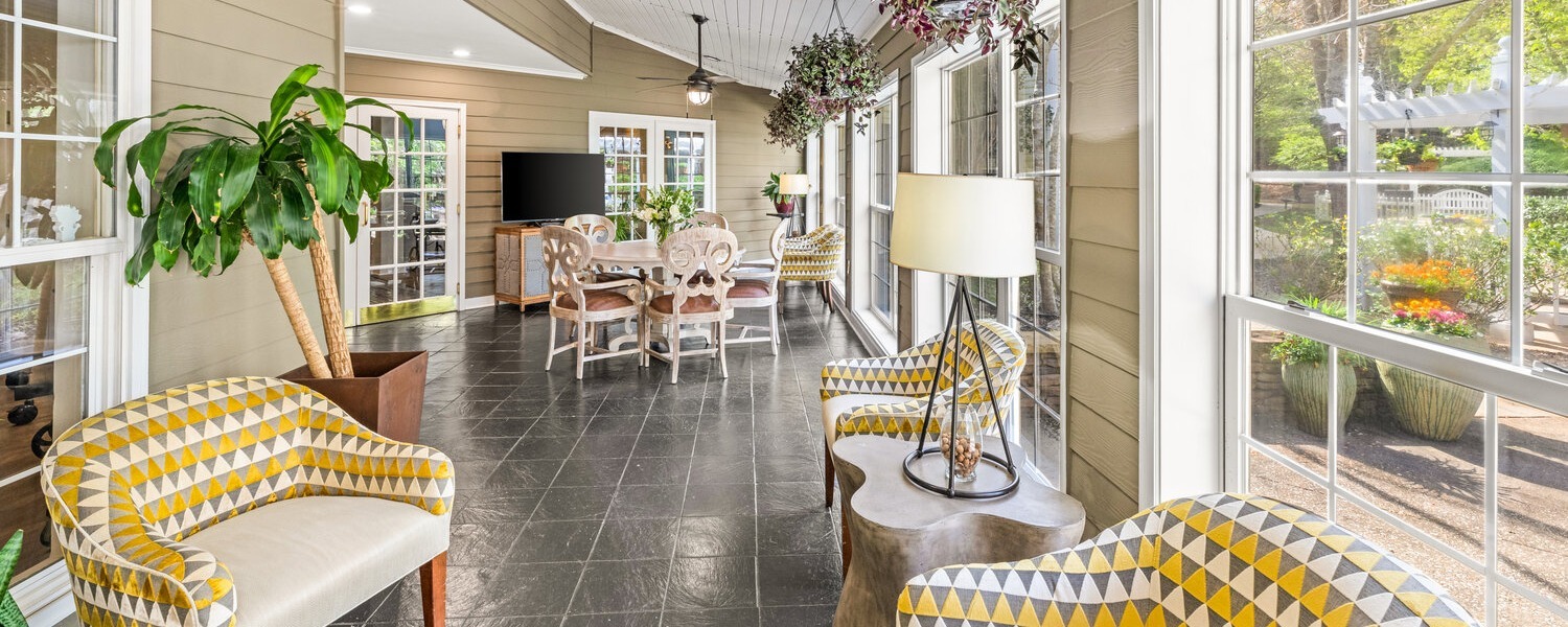 A bright, airy sunroom at Arbor Terrace Athens features patterned yellow accent chairs, hanging plants, and large windows overlooking a garden, offering a welcoming space for senior living in Athens, GA.