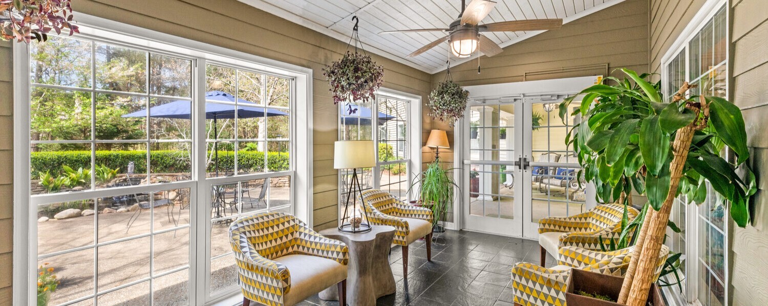 A sun-filled room at Arbor Terrace Athens with wicker seating, tall houseplants, large windows, and views of the outdoors — a bright, relaxing space ideal for active senior living in Athens, GA.
