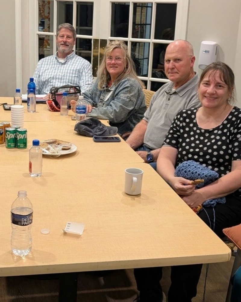 A group of family members gathers around a long table for an evening meeting at Arbor Terrace Athens, sharing refreshments and conversation at a senior living community in Athens, GA.