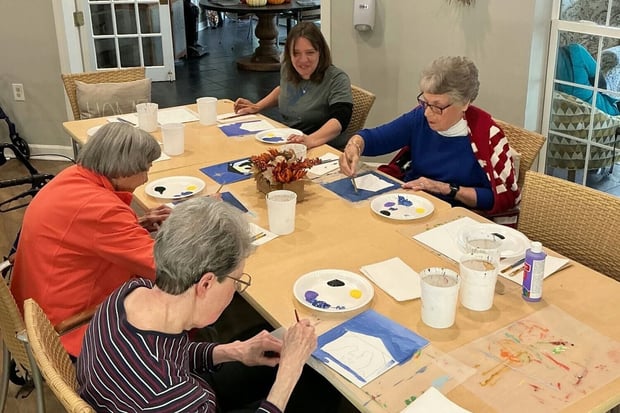 Residents and a staff member paint canvases together at a table at Arbor Terrace Athens, a senior living community in Athens, GA, reflecting engaging social engagement in Athens, GA.