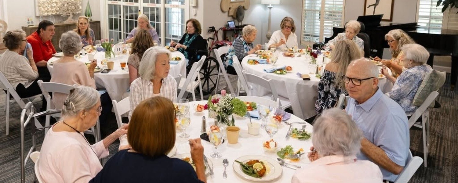 A lively dining event brings together residents, family members, and friends at a senior living community in Athens, GA, sharing meals around elegantly set tables in a bright, welcoming dining room.