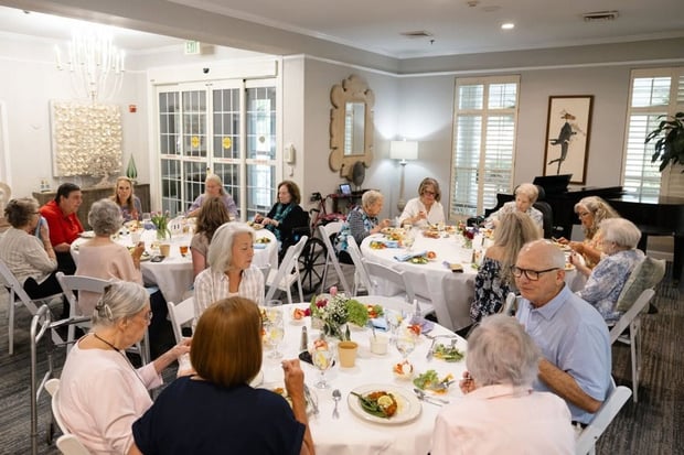 Residents and guests enjoy a festive dinner together in an elegantly decorated dining room at a senior living community in Athens, GA, with floral centerpieces and warm lighting.