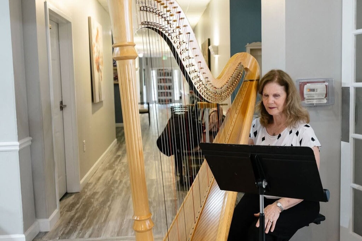 A harpist performs in a sunlit hallway, bringing live musical entertainment to residents at Arbor Terrace Athens.