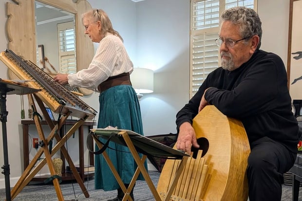Two musicians perform live on a hammered dulcimer and a stringed instrument for residents at a senior living community in Athens, GA, bringing folk music entertainment to the community.