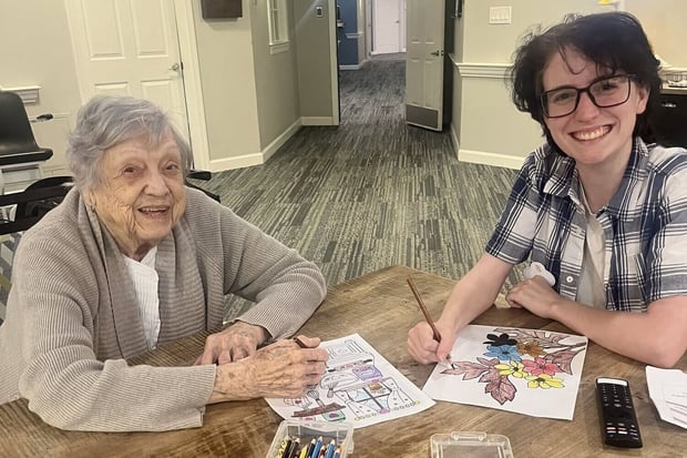 A resident and a staff member share a joyful moment while coloring together at a table at a senior living community in Athens, GA, with colored pencils and artwork spread between them.