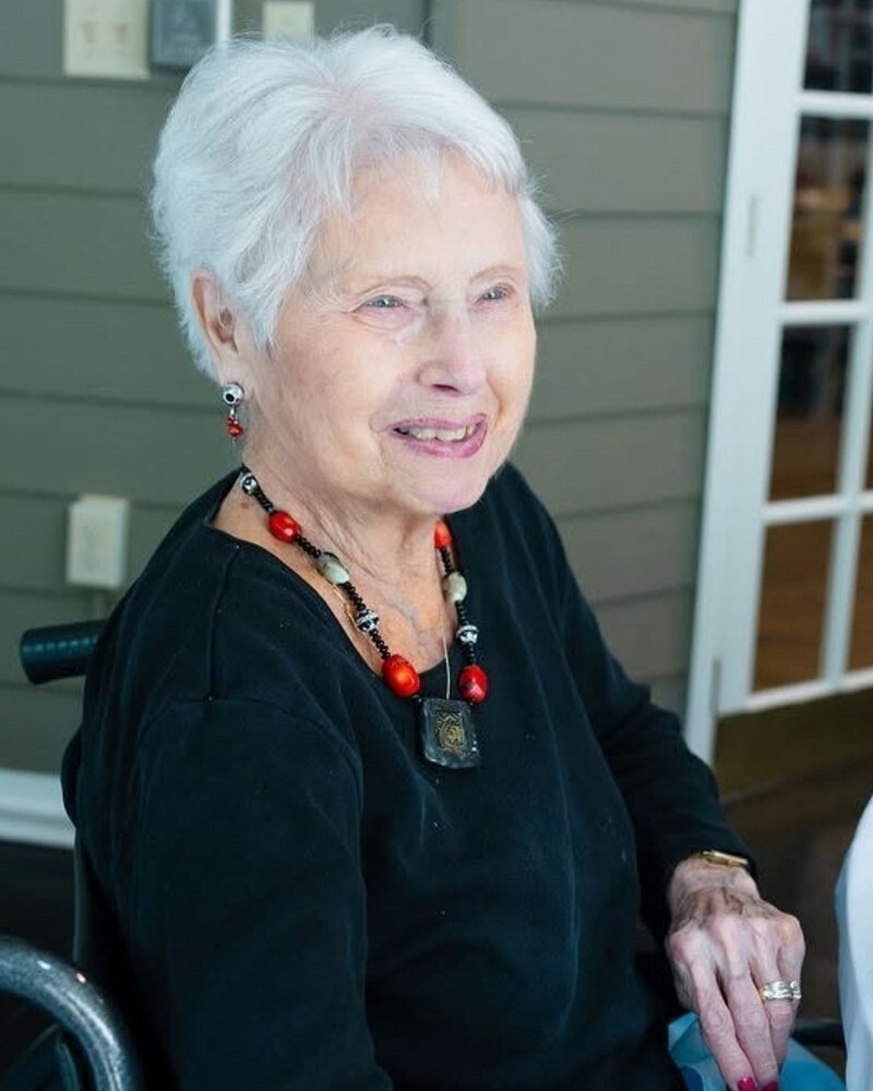 A resident smiles warmly while seated outdoors on the patio at Arbor Terrace Athens, enjoying the fresh air at a senior living community in Athens, GA.