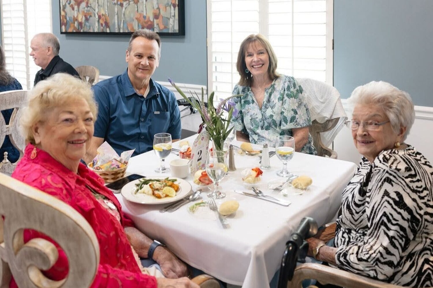 Residents share a meal with visiting family at a table set with fresh flowers at Arbor Terrace Athens, a senior living community in Athens, GA, reflecting warm social engagement in Athens, GA.