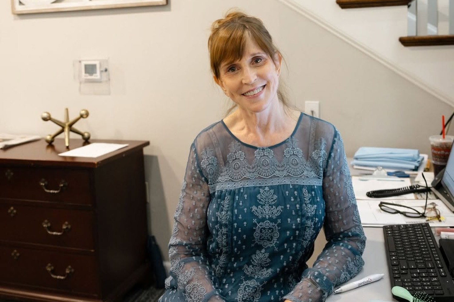 A staff member smiles warmly from behind a desk in the office at Arbor Terrace Athens, a senior living community in Athens, GA.