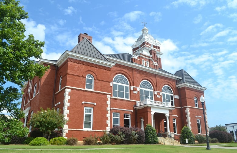 A red brick historic courthouse with a clock tower under a blue sky near Monroe, GA, close to Arbor Terrace Athens, offering assisted living near Monroe, GA and senior living in Athens, GA.