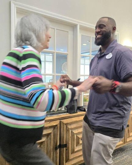 A resident and a staff member share a joyful dance together in a bright, welcoming common area at Arbor Terrace Athens, a senior living community in Athens, GA.