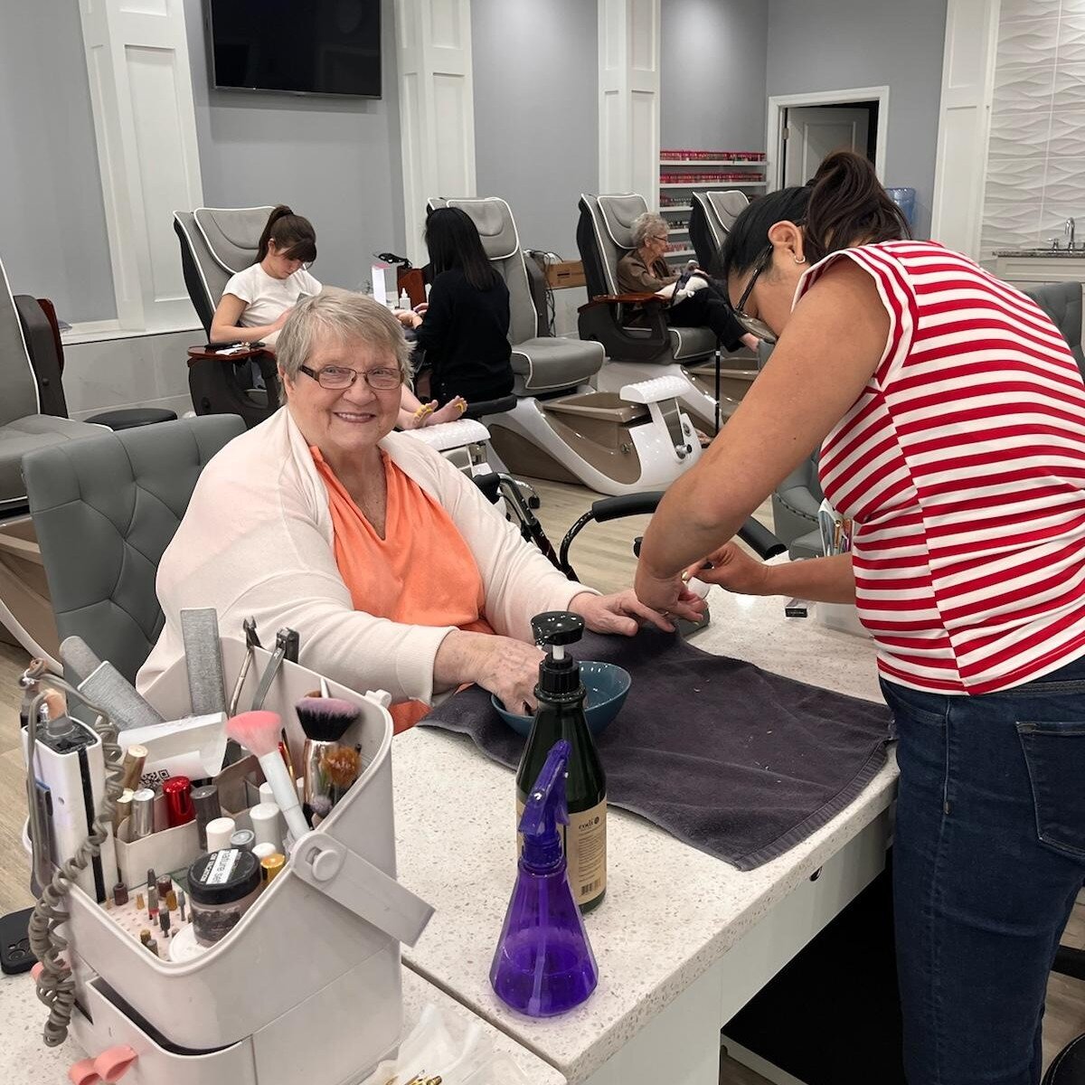 A resident enjoying a nail care service at Arbor Terrace Athens, smiling as a staff member attends to her, reflecting the personalized amenities offered at this senior living community in Athens, GA.