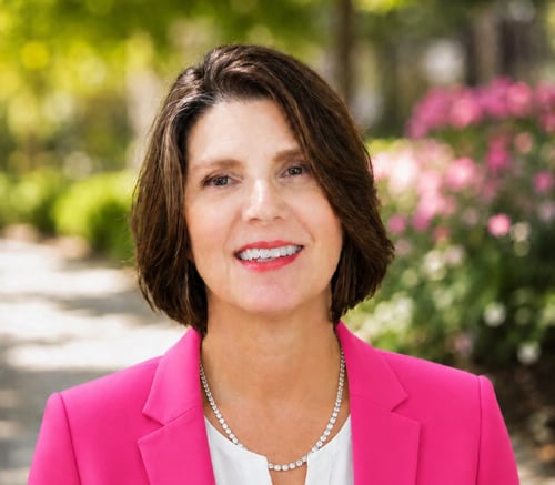 A smiling staff member at Arbor Terrace Athens, a senior living community in Athens, GA, photographed outdoors with blooming pink flowers in the background.