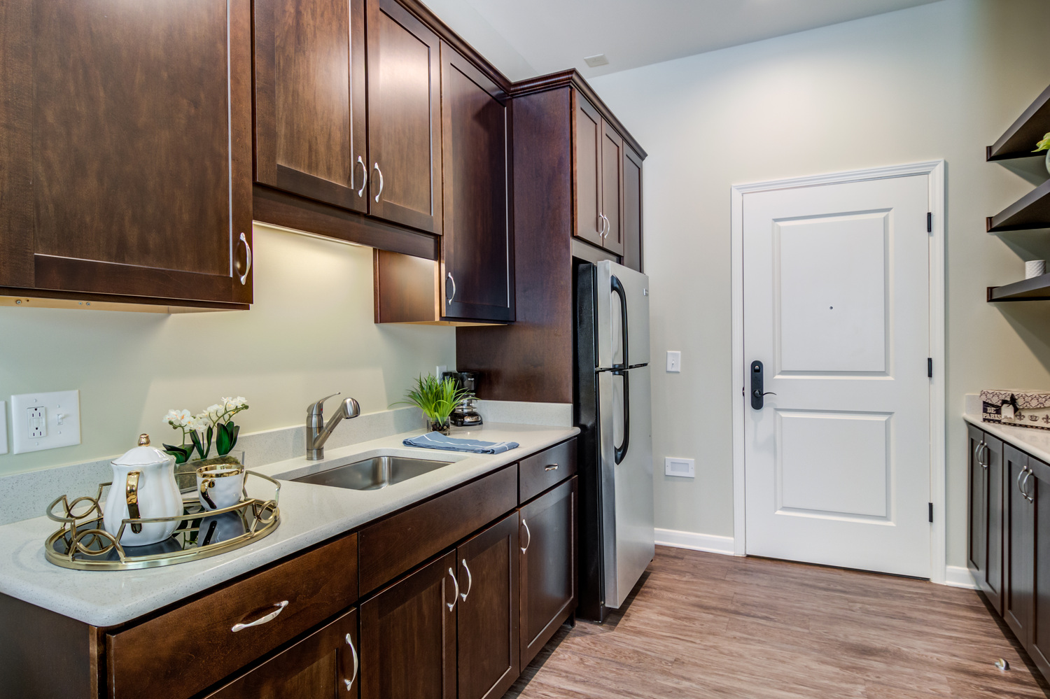 A well-appointed apartment kitchen featuring rich dark wood cabinetry, light stone countertops, stainless steel appliances, and warm hardwood floors at Arbor Terrace Burnt Hickory, a senior living community in Marietta, GA.