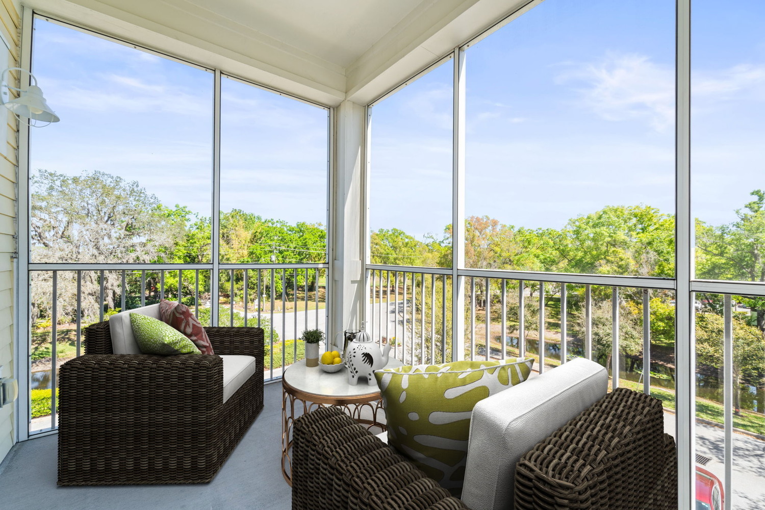 A bright screened-in balcony at Arbor Terrace Citrus Park, featuring wicker seating, colorful accent pillows, and sweeping views of mature trees, perfect for enjoying the Florida sunshine in senior living in Tampa, FL.