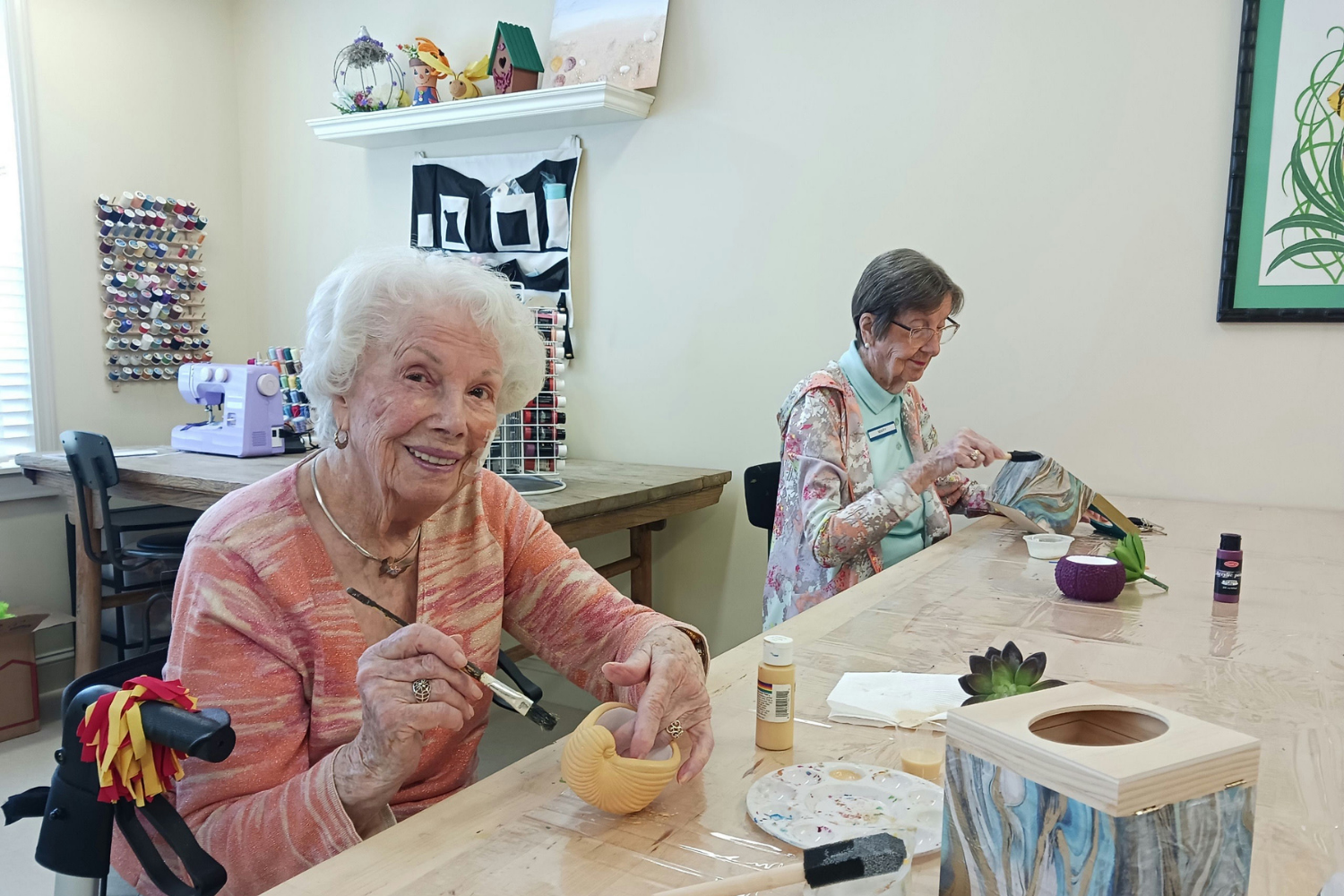 Smiling residents enjoy a creative painting and crafts session in a bright art studio, showcasing the engaging activities offered at senior living near Carrollwood, FL.