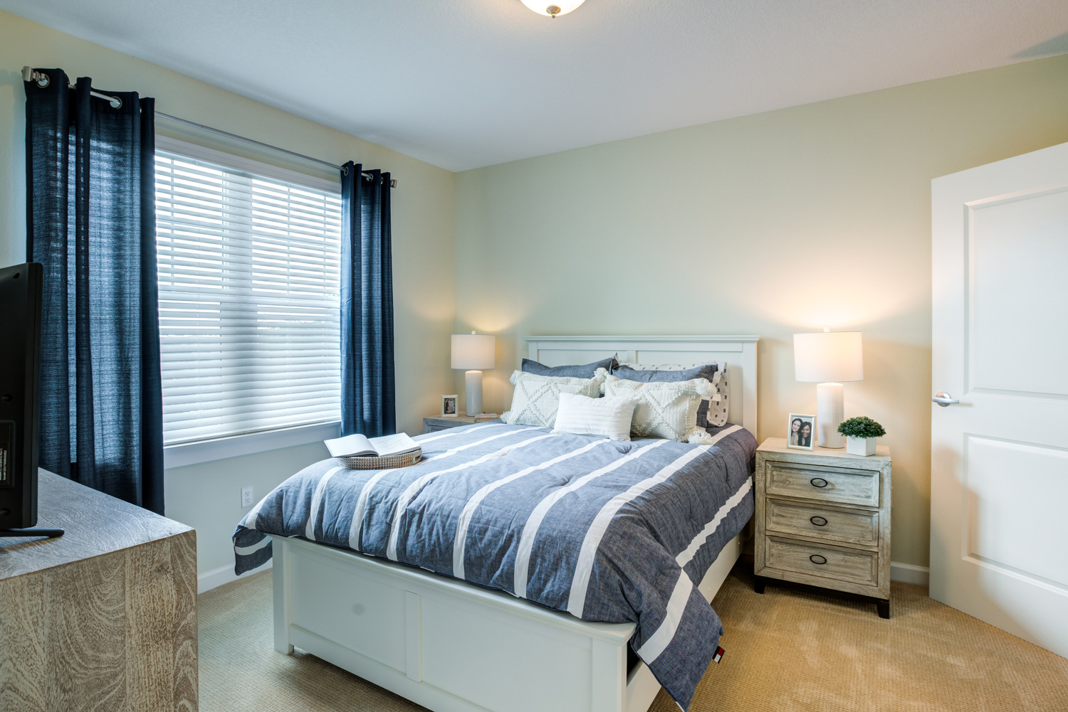 A cozy apartment bedroom at Arbor Terrace Citrus Park features navy drapes, soft bedding, and warm lighting, creating a peaceful and homey retreat for residents enjoying senior living in Tampa, FL.