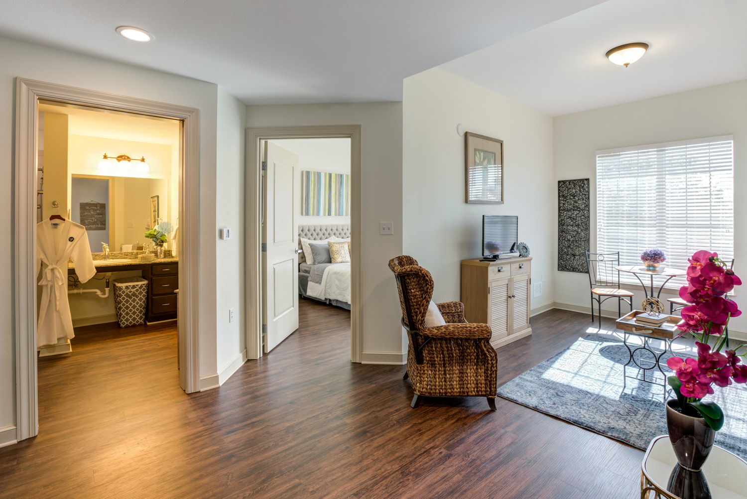 A spacious apartment at Arbor Terrace Citrus Park showcases rich hardwood floors, a sunlit sitting area, and open views into the bedroom and bathroom, offering comfortable independent living in Tampa, FL.