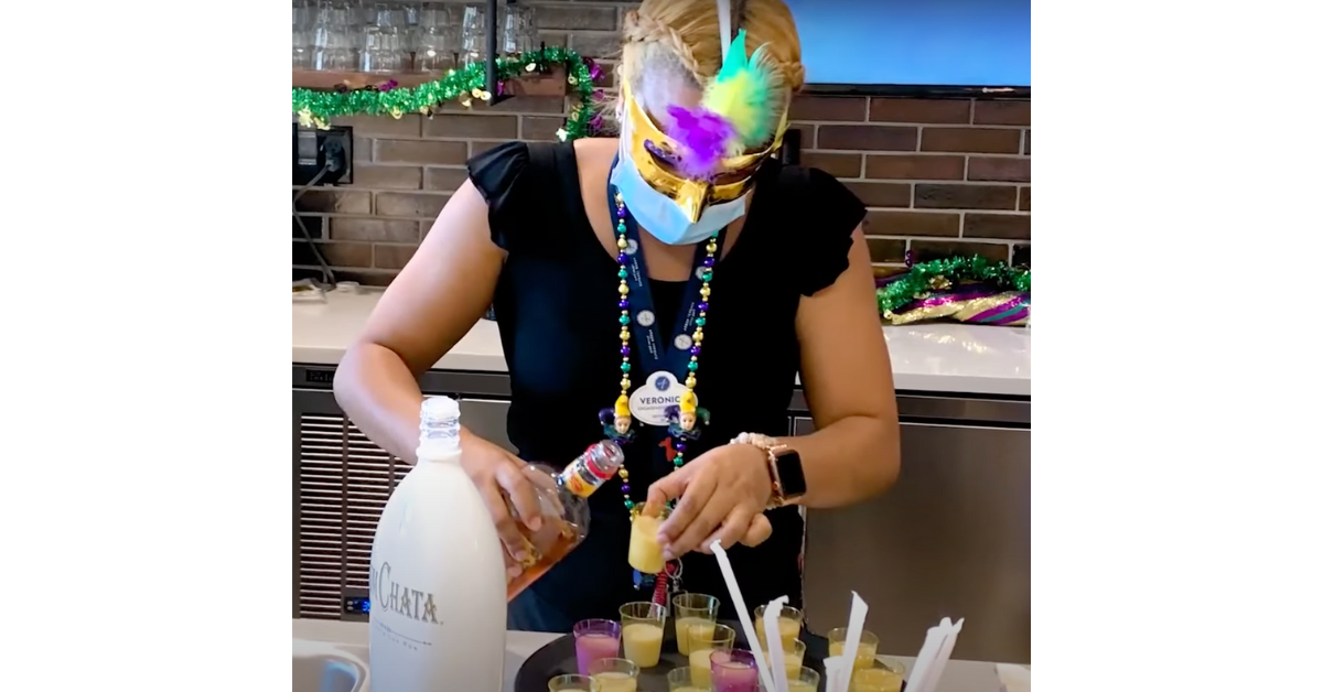 A staff member in festive Mardi Gras attire pours colorful drinks during a lively themed celebration at senior living in Citrus Park, FL.