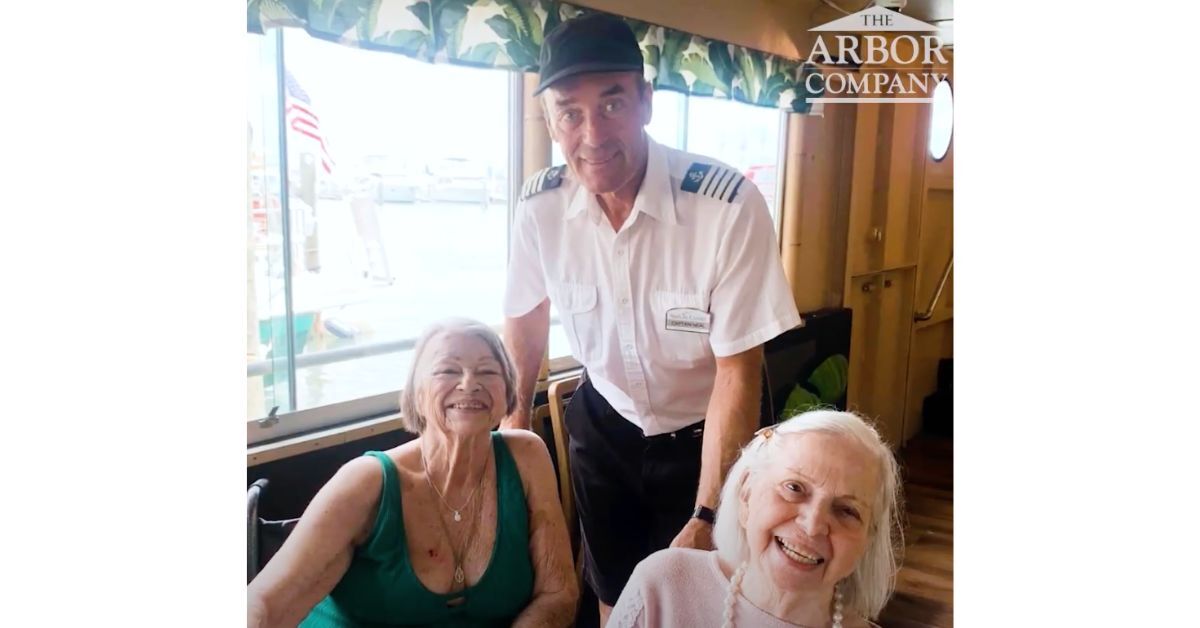 Two residents smile alongside a boat captain during a waterfront outing, capturing the vibrant, active senior living near the Tampa Bay waterfront.