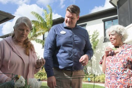 A staff member helps two residents tend to fresh tulips in a garden bed outside, reflecting the engaging, hands-on activities at senior living in Cooper City, FL, and senior living near parks and recreation in Cooper City, FL.
