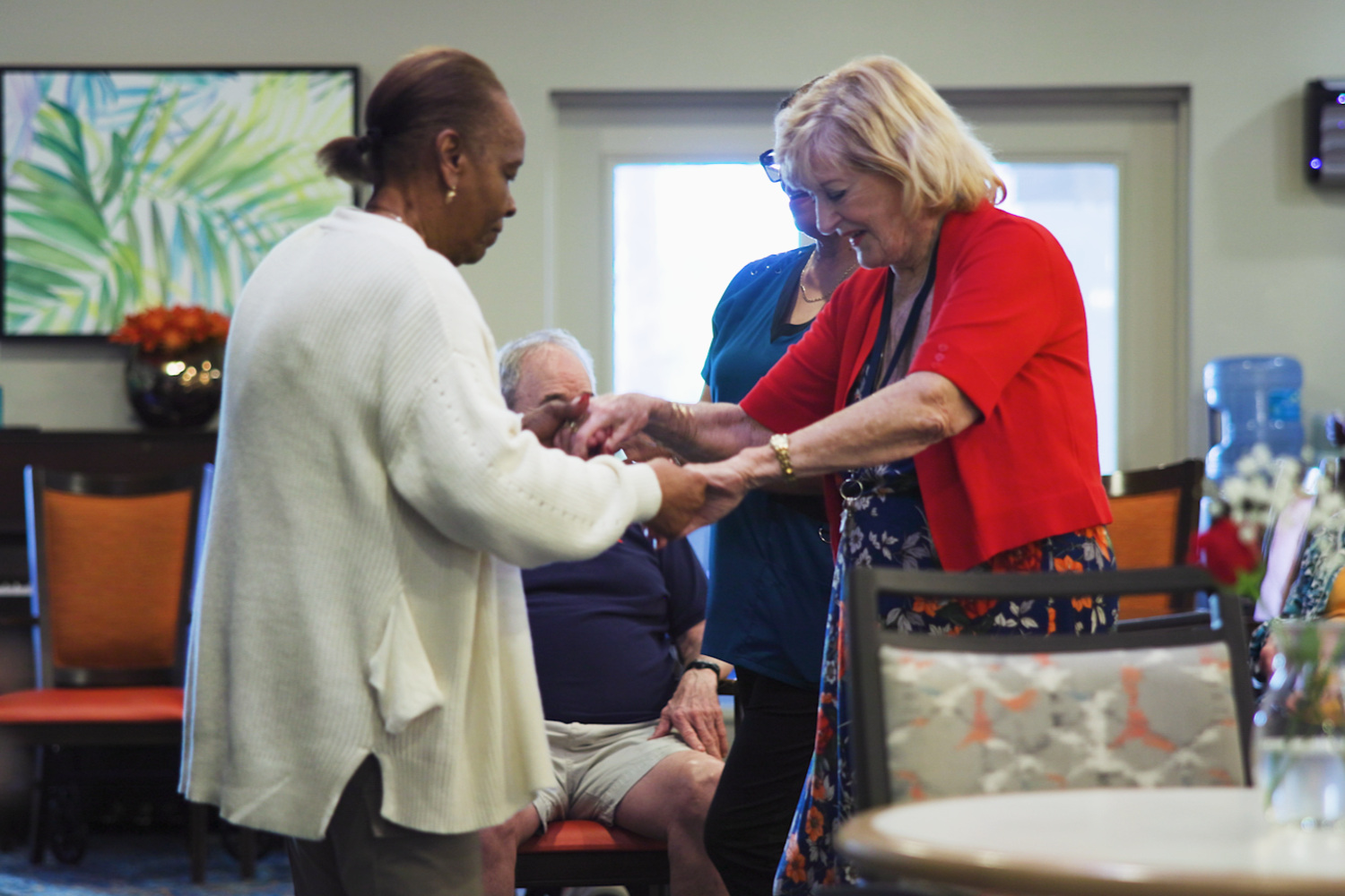 A staff member helps a resident while another woman looks on warmly, reflecting the caring community connection at The Arbor Company.
