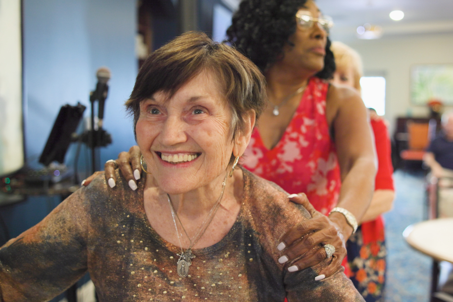 A group of women share a warm, joyful moment together indoors, reflecting the friendship and active senior lifestyle at The Arbor Company.