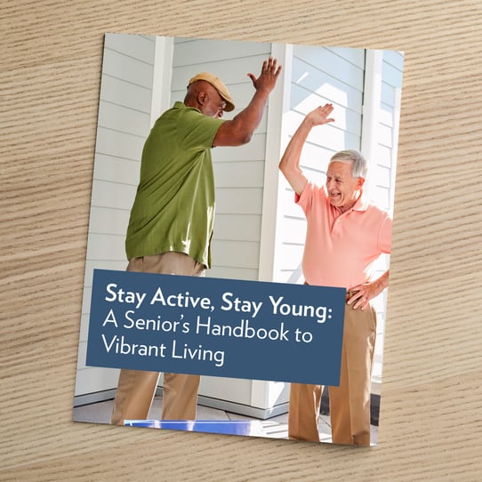 A booklet titled "Stay Active, Stay Young: A Senior's Handbook to Vibrant Living" resting on a wooden surface, featuring a photo of two older men dancing joyfully outdoors.