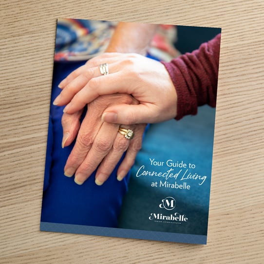 Cover of 'Your Guide to Connected Living at Mirabelle,' showing a close-up of one hand resting gently on top of an older adult's hand, with the Mirabelle Senior Living logo below.
