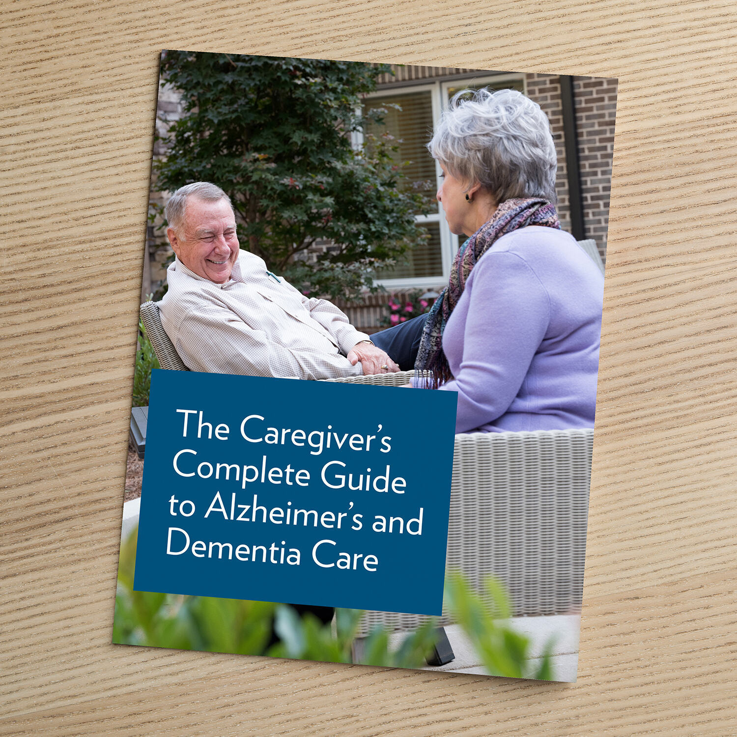 Cover of a brochure titled "The Caregiver's Complete Guide to Alzheimer's and Dementia Care," featuring an older man and a woman seated outdoors, sharing a warm conversation.