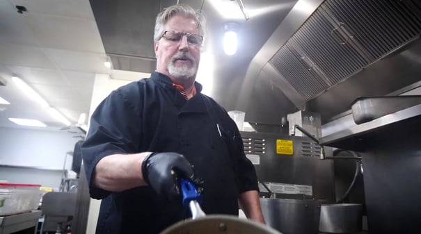 a chef flipping a pan in a professional kitchen of a senior living community
